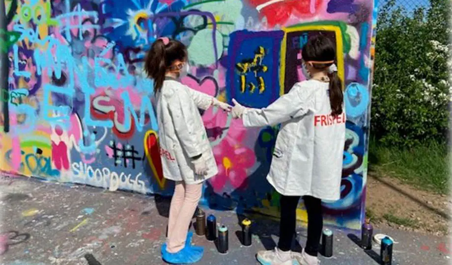 Två flickor i vita rockar framför vägg med grafitti